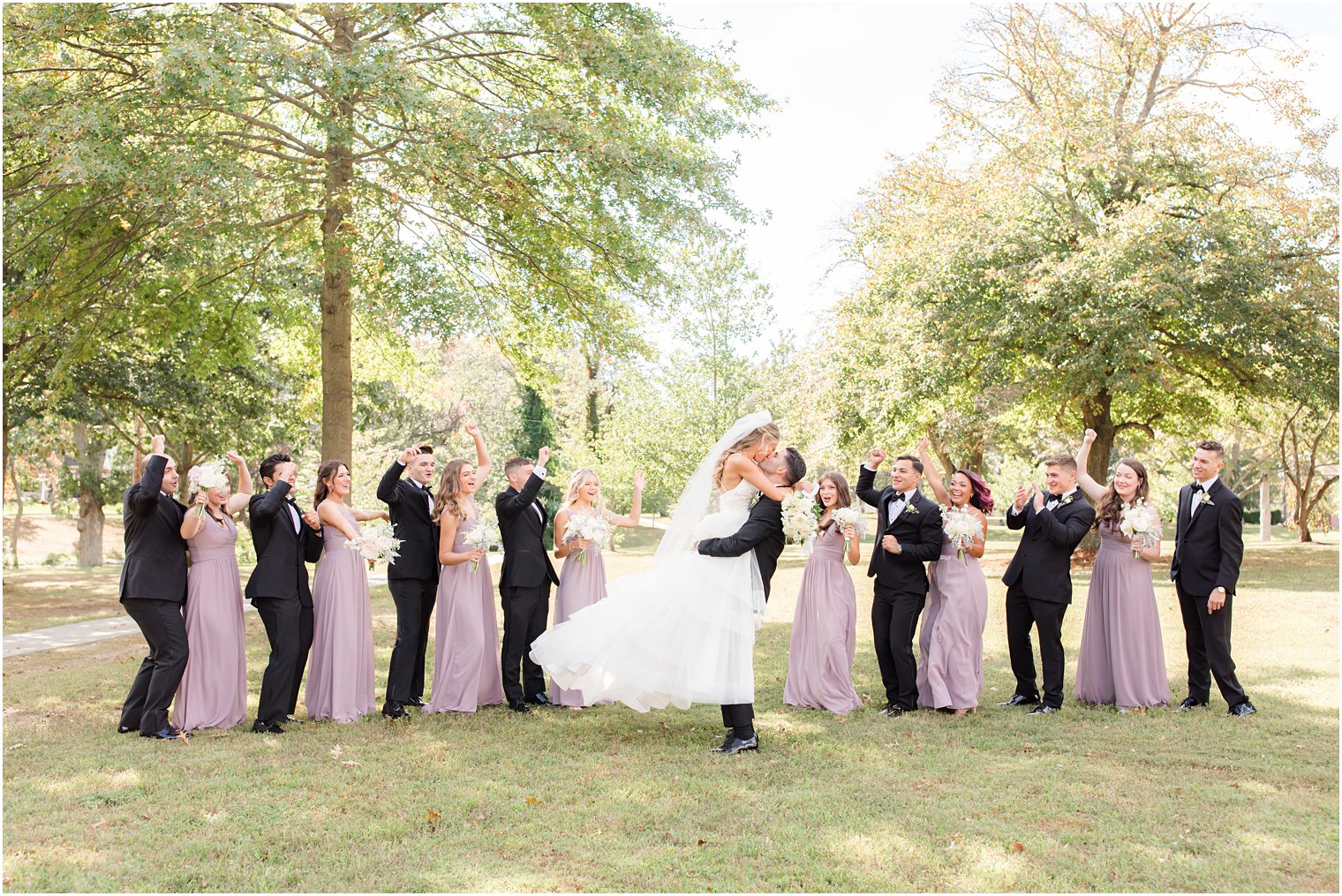 groom lifts bride up with wedding party behind them