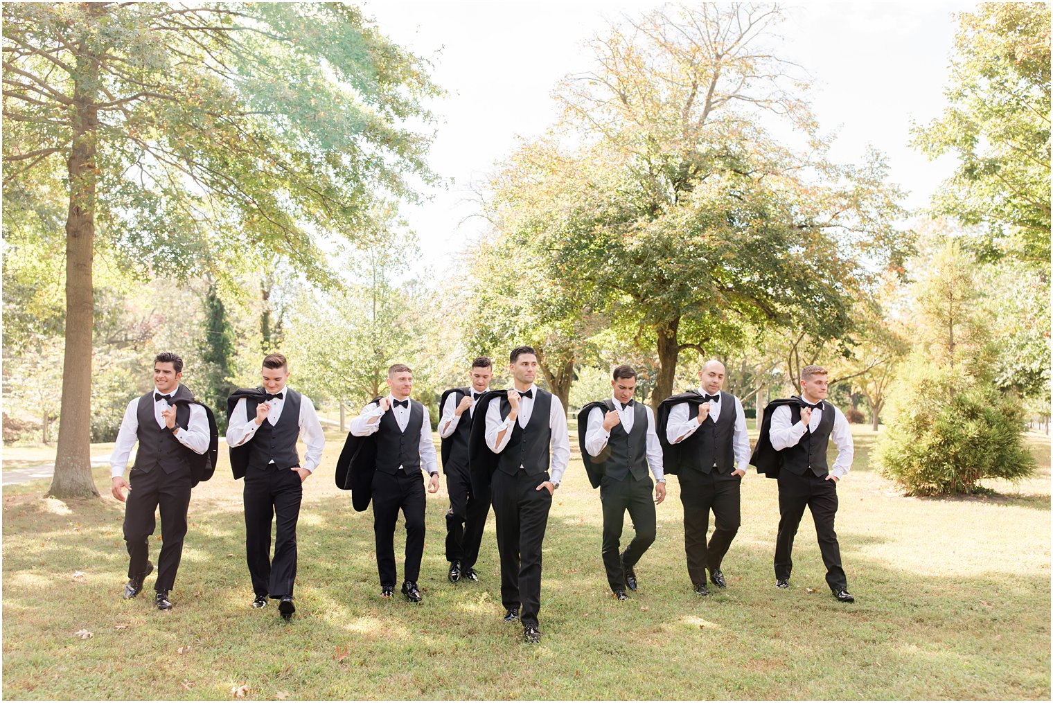 groom walks with groomsmen in black suits with jackets over shoulder