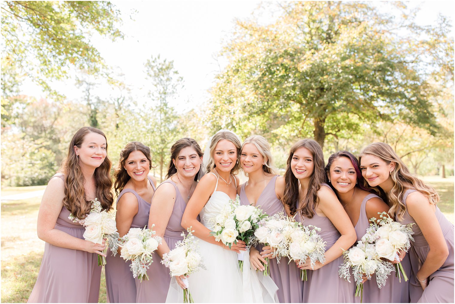 bride poses with bridesmaids in purple gown with light white flowers