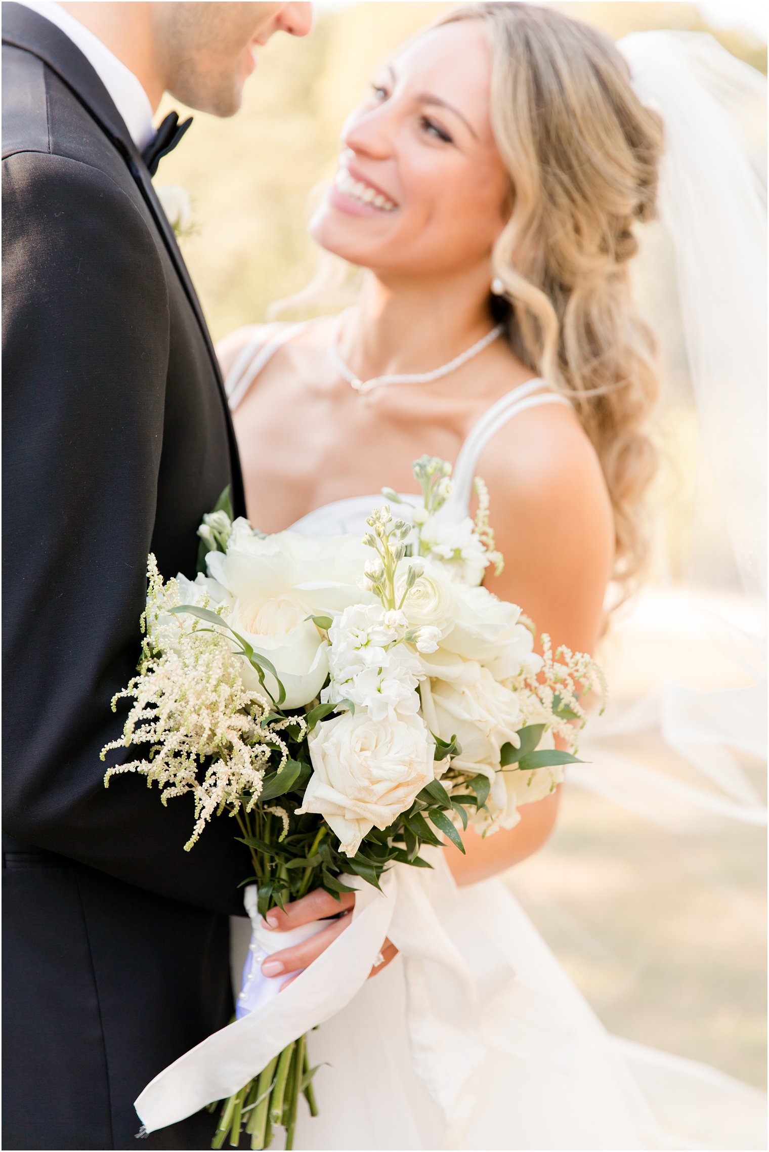 newlyweds smile while bride holds bouquet of ivory flowers