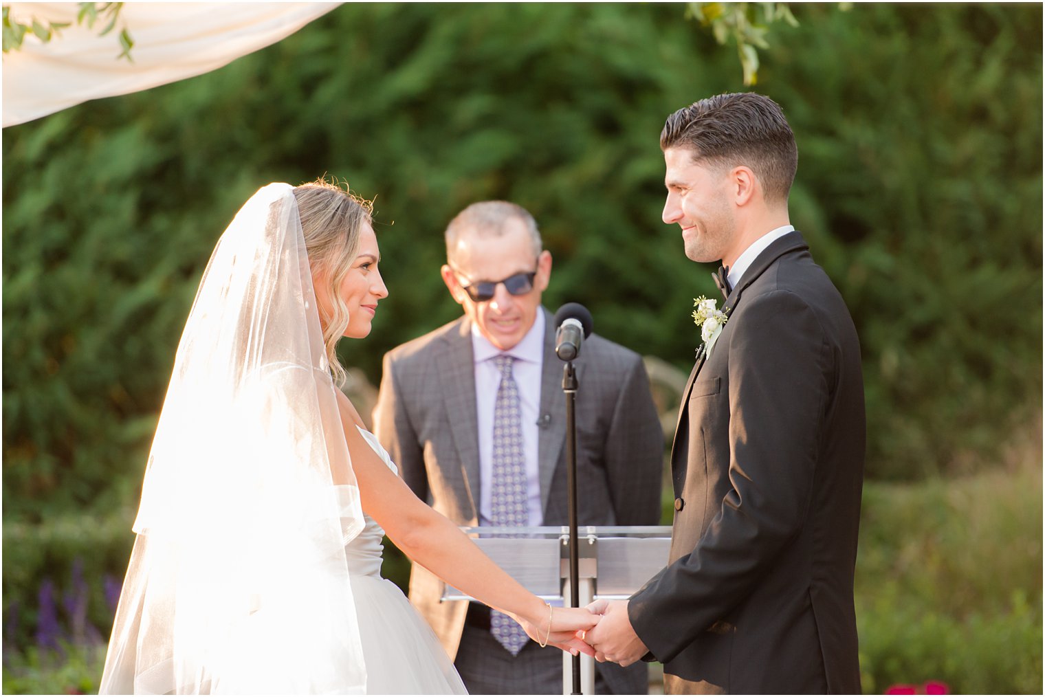 newlyweds hold hands smiling together during ceremony at the Mill Lakeside Manor