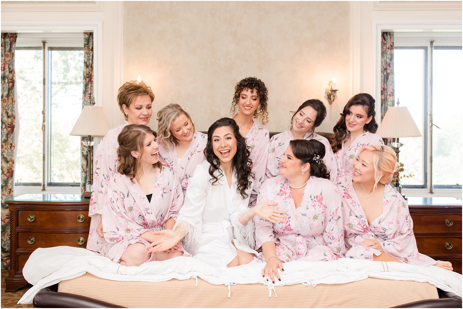 bridesmaids in pastel pink robes sit on bed before Village Club of Sands Point wedding
