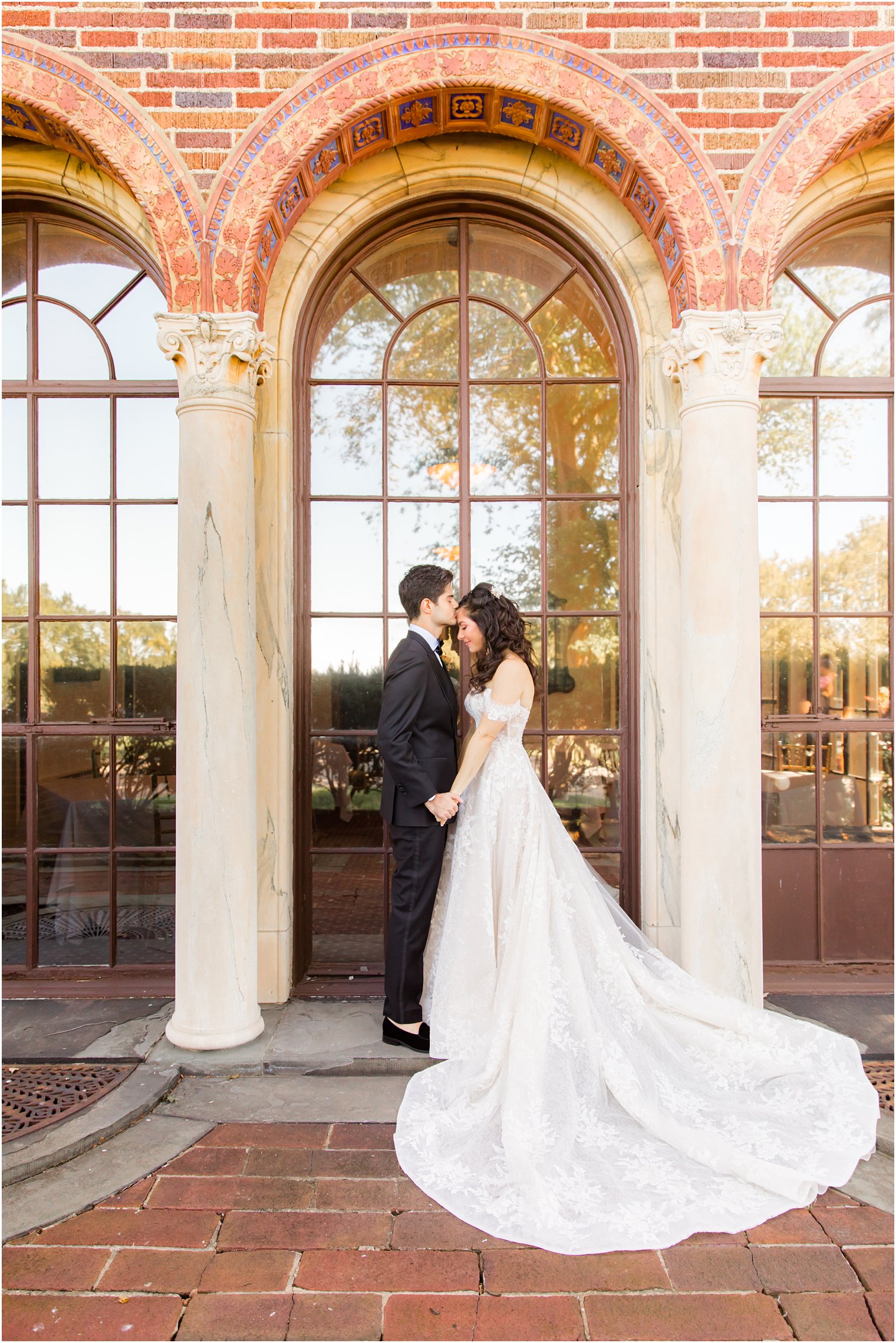 groom holds bride's hands and kisses her forehead outside Village Club of Sands Point