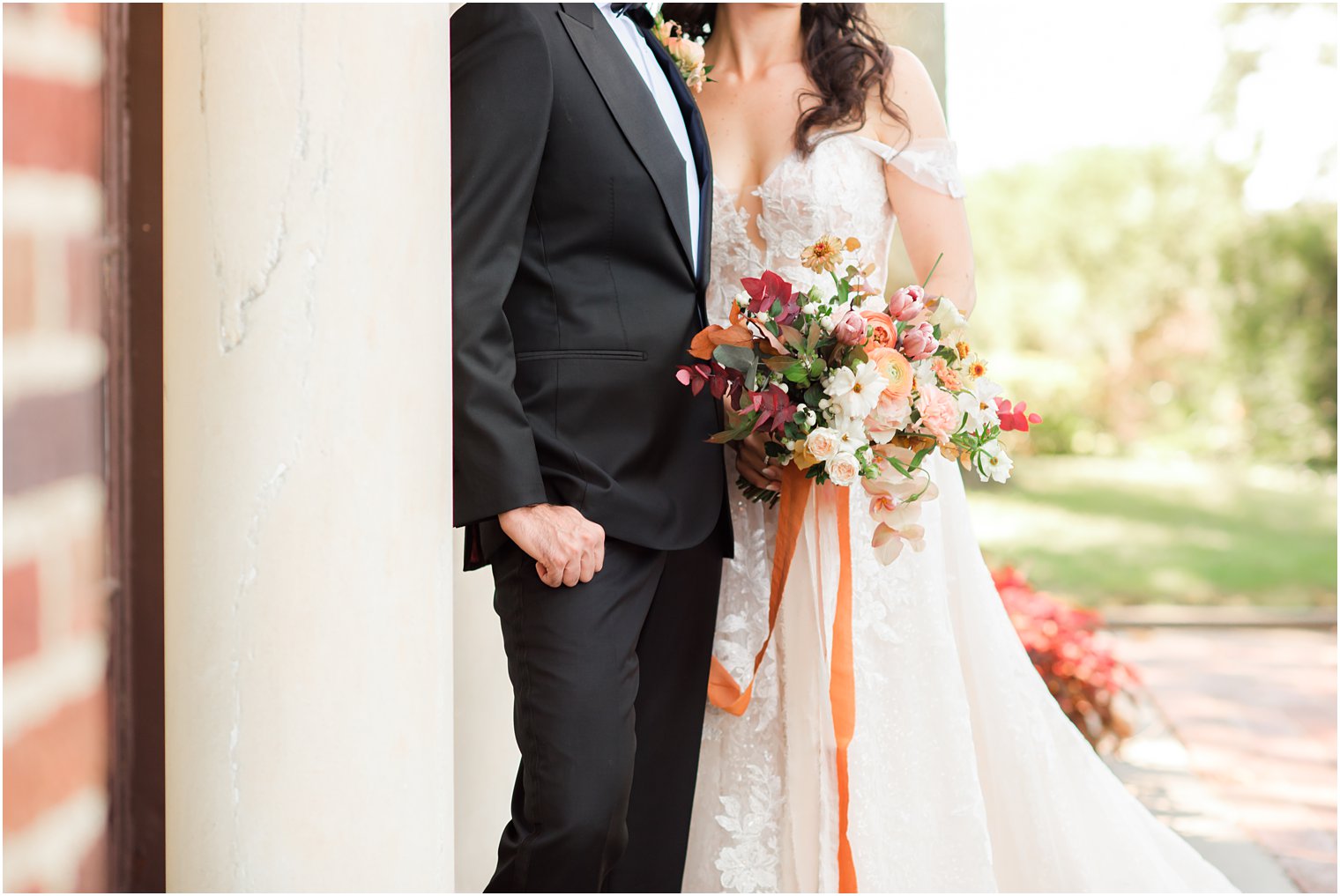bride holds bouquet of fall flowers with long orange ribbon