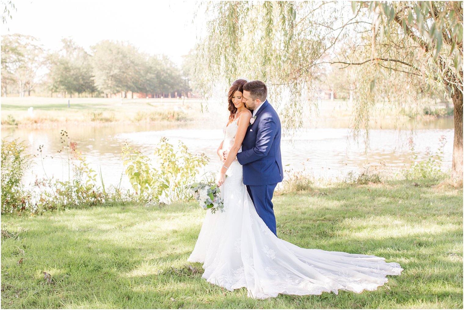 groom hugs bride during Princeton NJ wedding portraits by lake at Chauncey Hotel