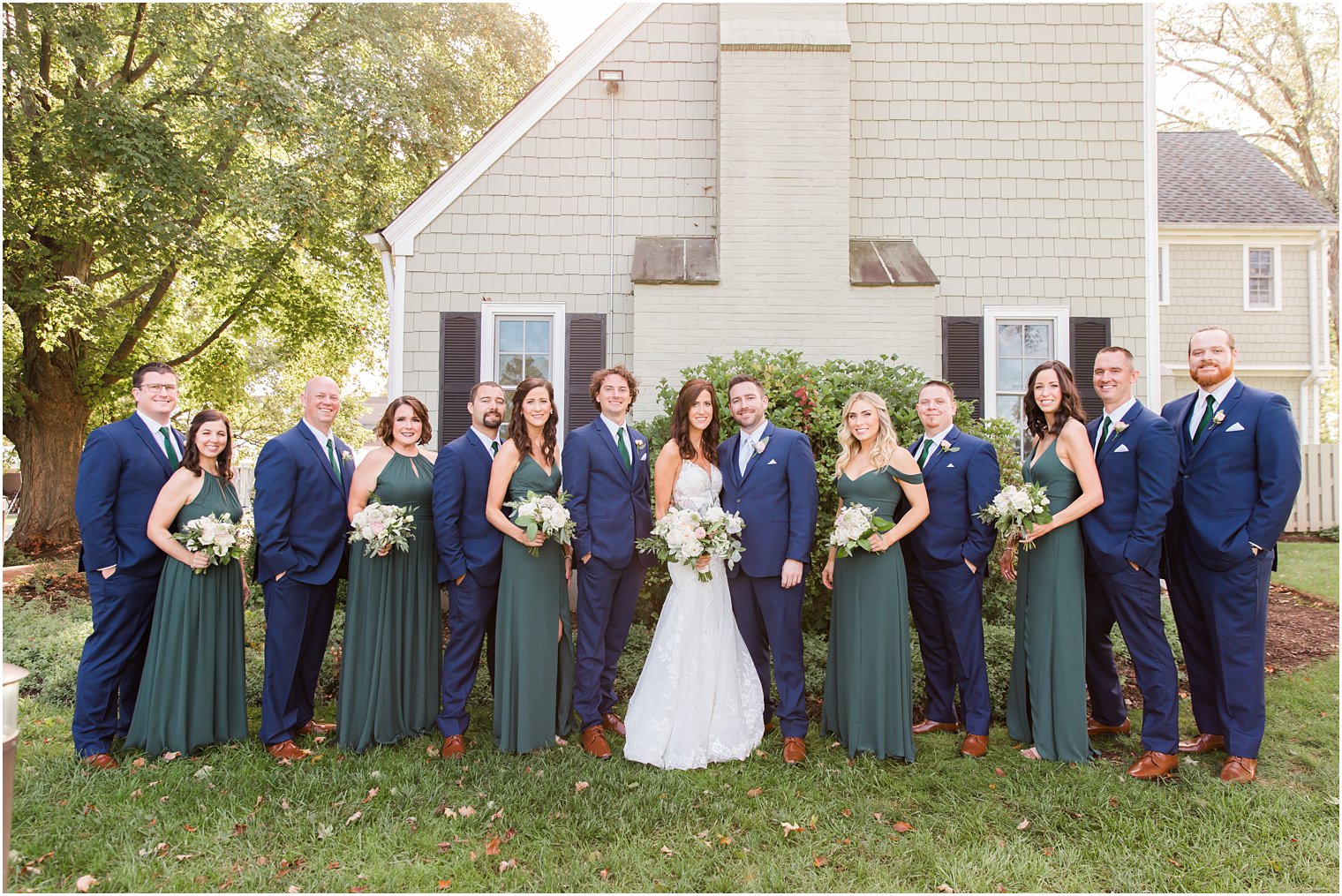 bridal party in navy and green attire poses with bride and groom on wedding day 