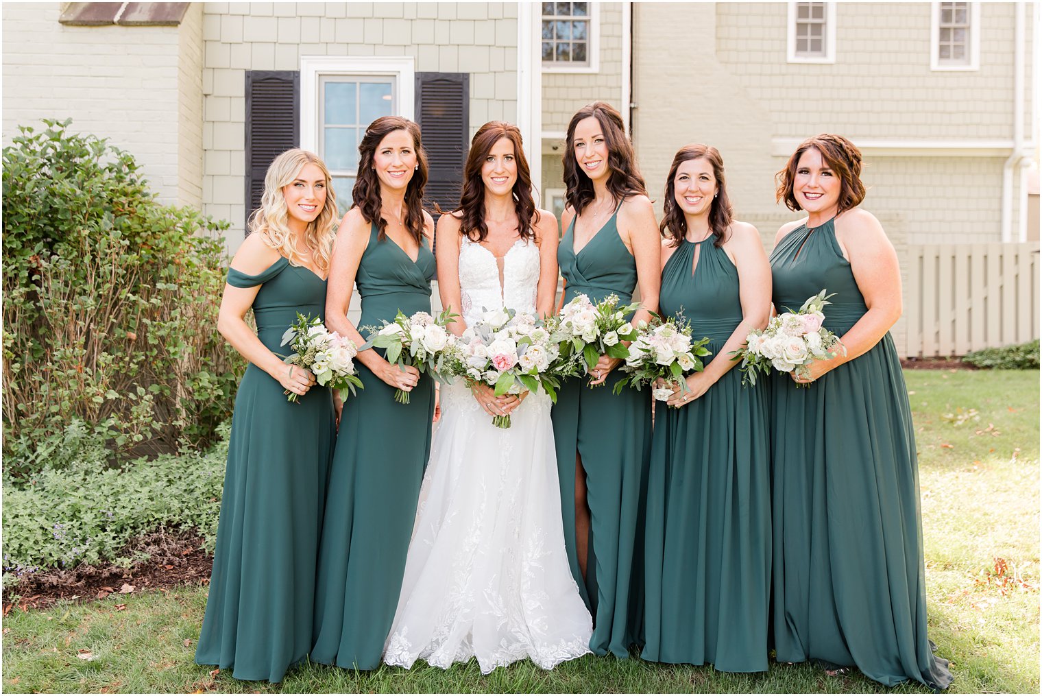 bride stands with bridesmaids in emerald green gowns for fall wedding 