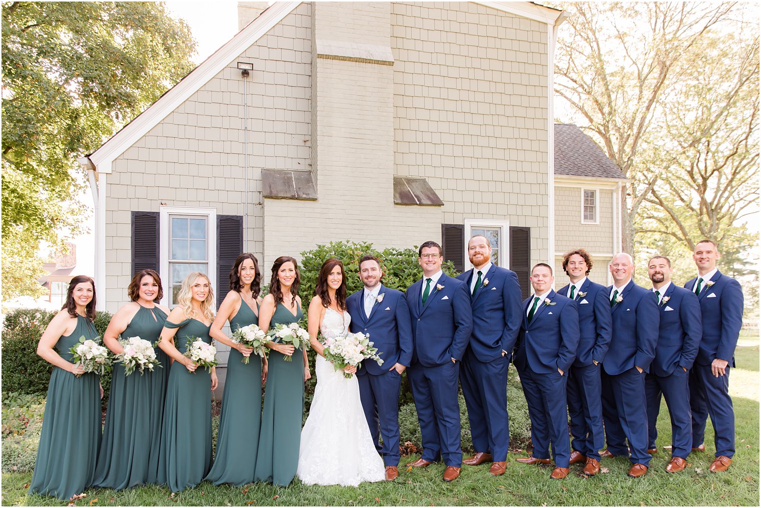 bride and groom pose with wedding party in emerald green dresses and navy suits 
