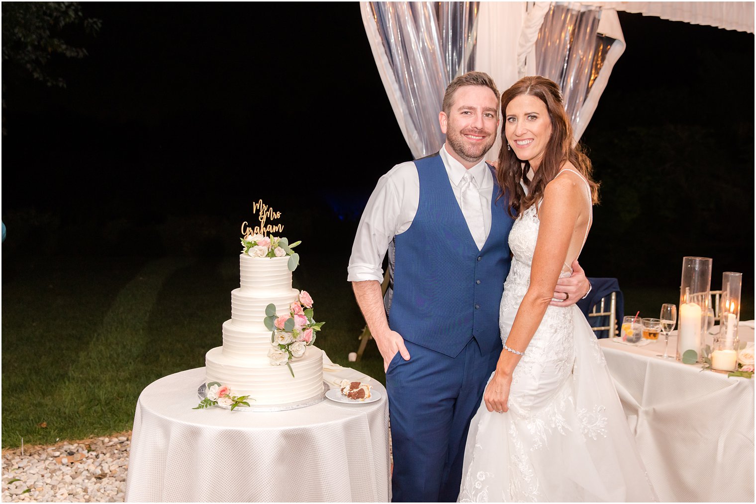 newlyweds pose by tiered wedding cake during tented wedding reception in Princeton NJ