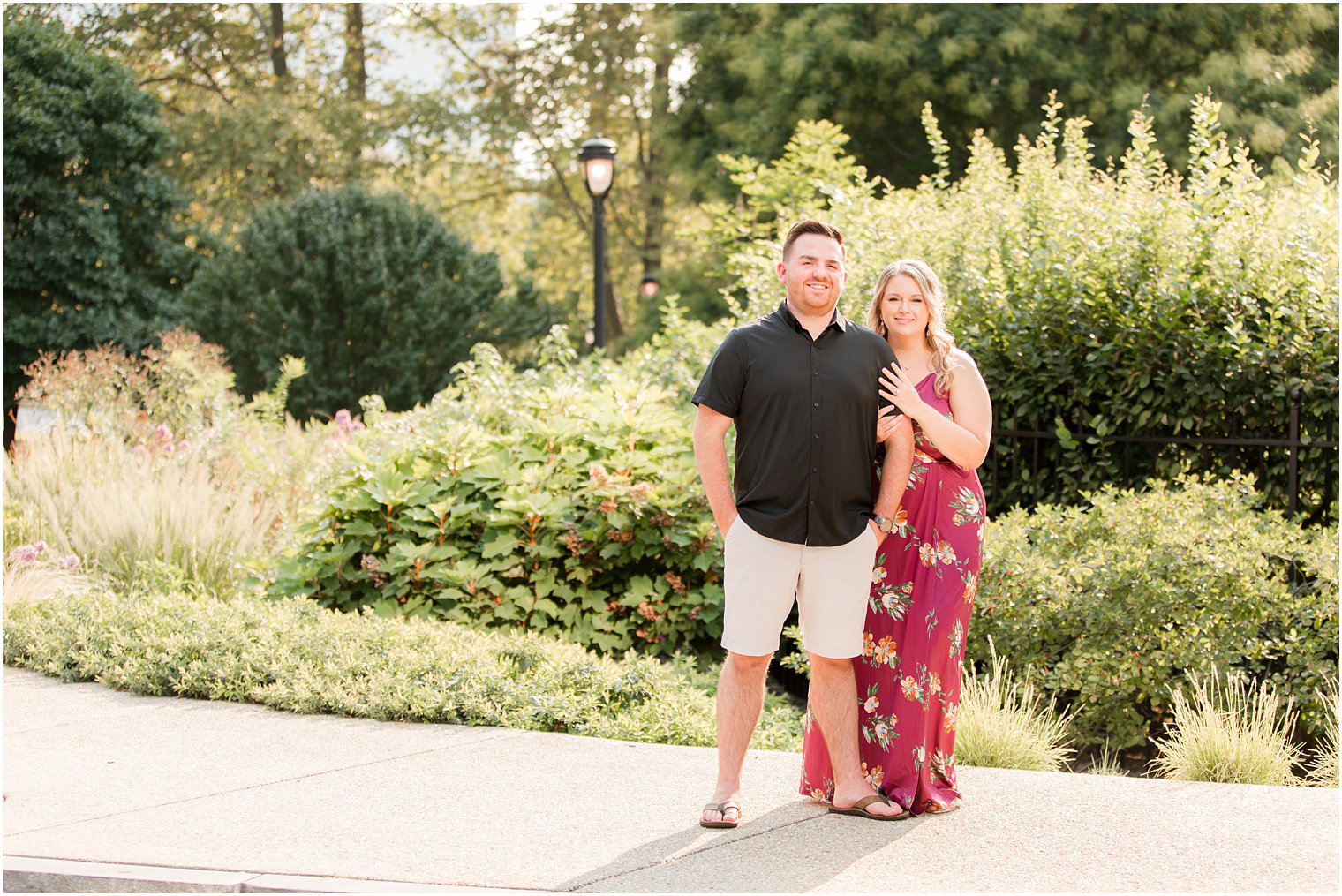 bride stands behind groom holding his arm during engagement photos in Philly, PA