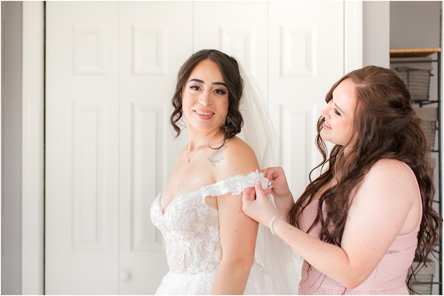 bridesmaid in pink gown helps bride with wedding dress 