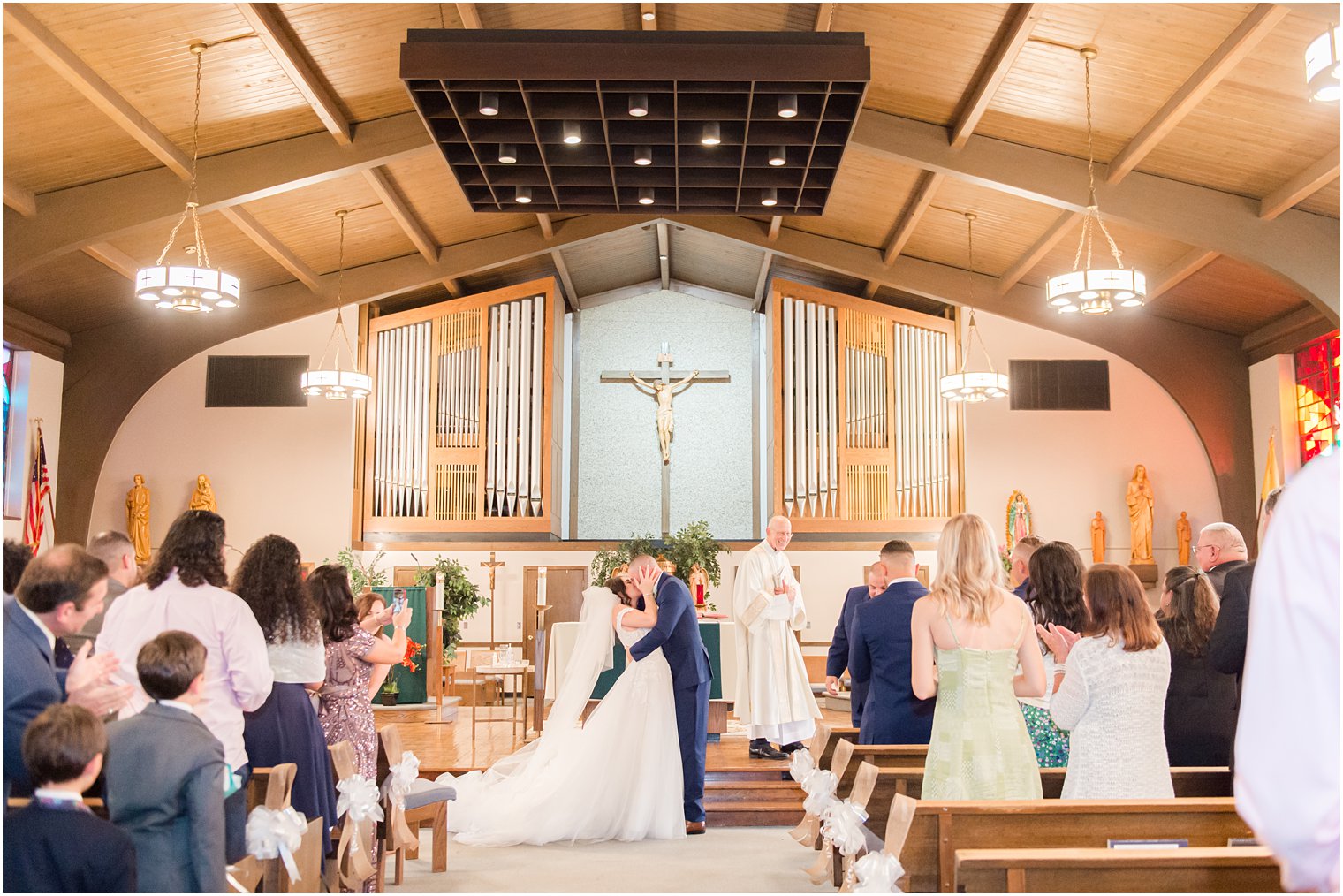 guests clap for bride and groom's first kiss during traditional wedding ceremony at Saint Matthew the Apostle church