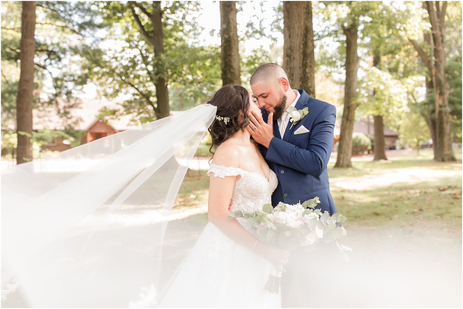 bride and groom stand touching noses with veil pulled around them 