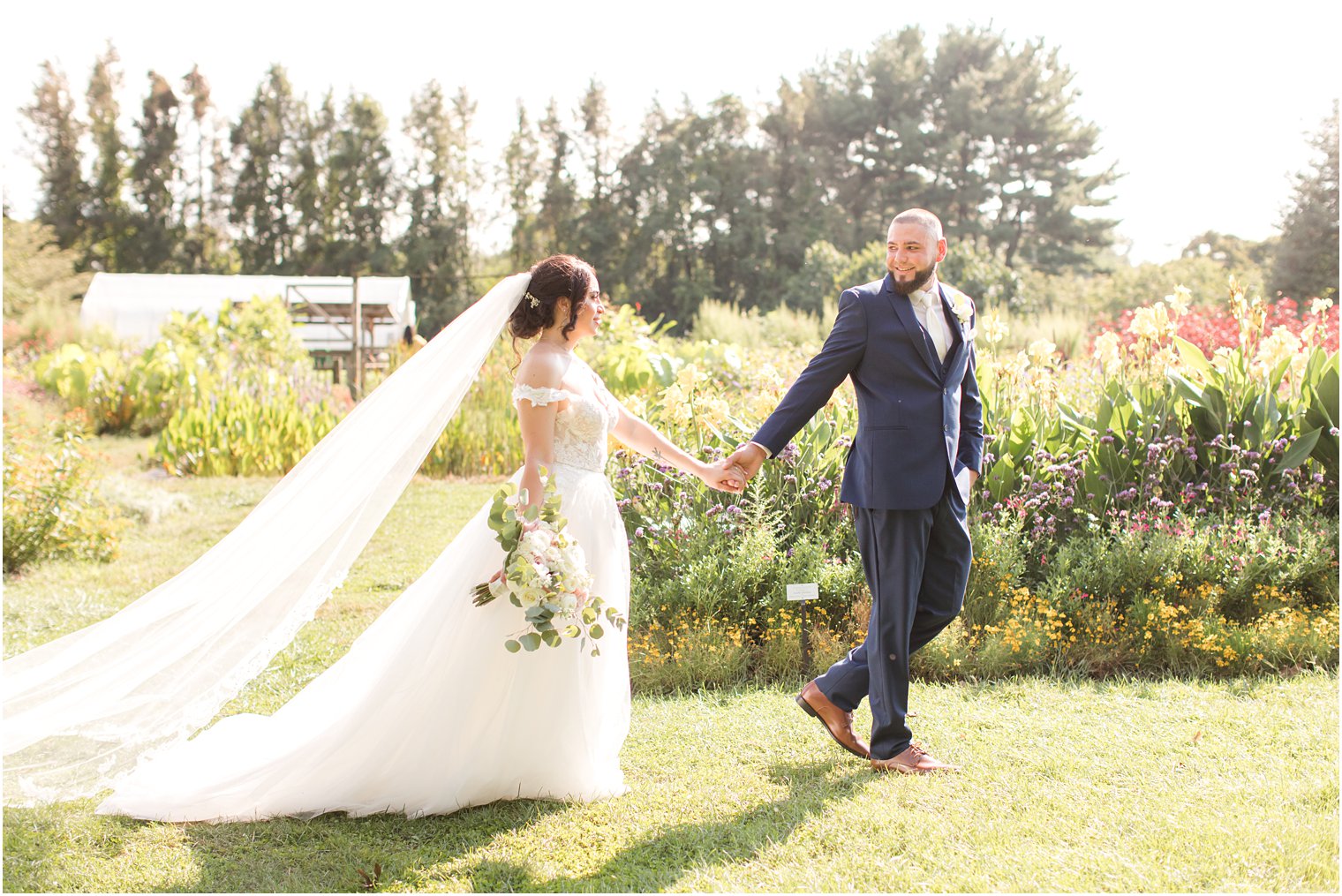 newlyweds hold hands walking through Rutgers Gardens on wedding day 