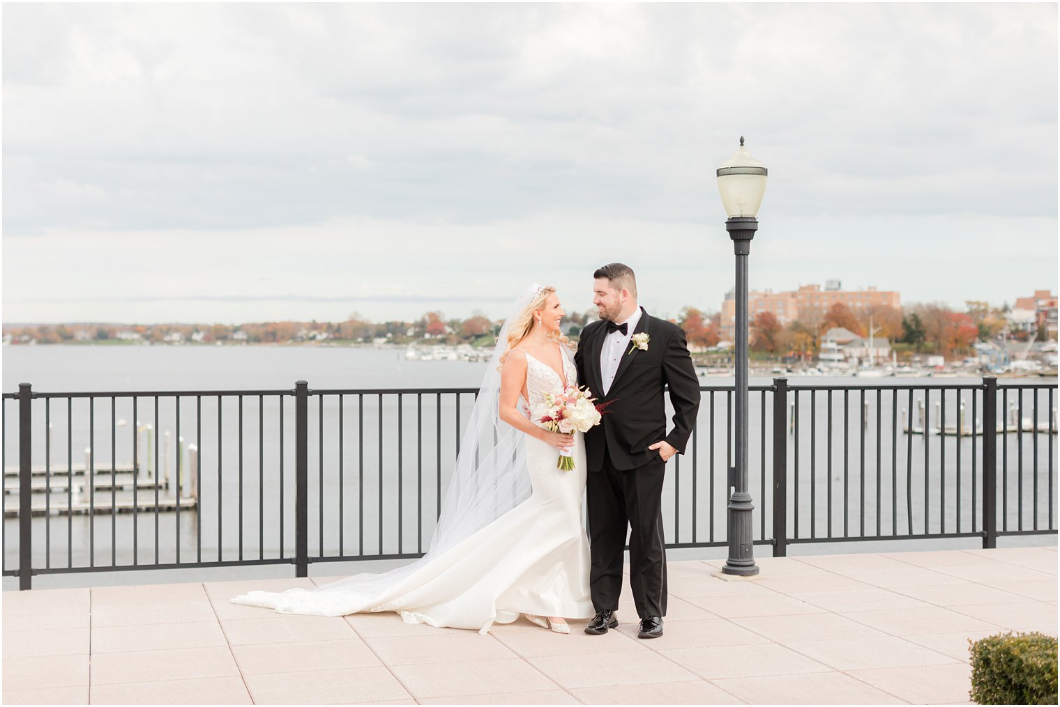 bride looks up at groom with veil behind her in front of water at the Molly Pitcher Inn