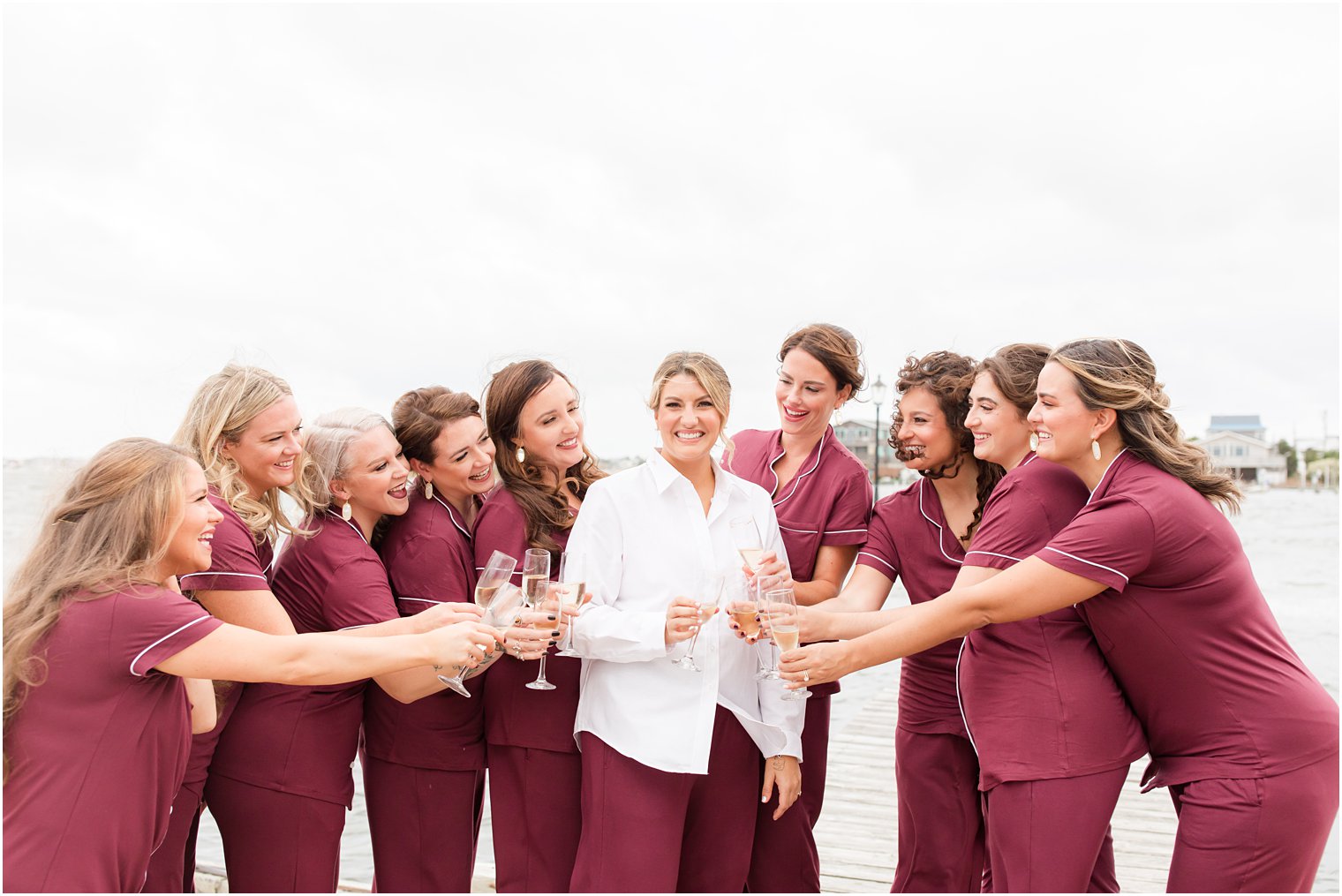 bride smiles with bridesmaids in matching burgundy pajamas toasting champagne 