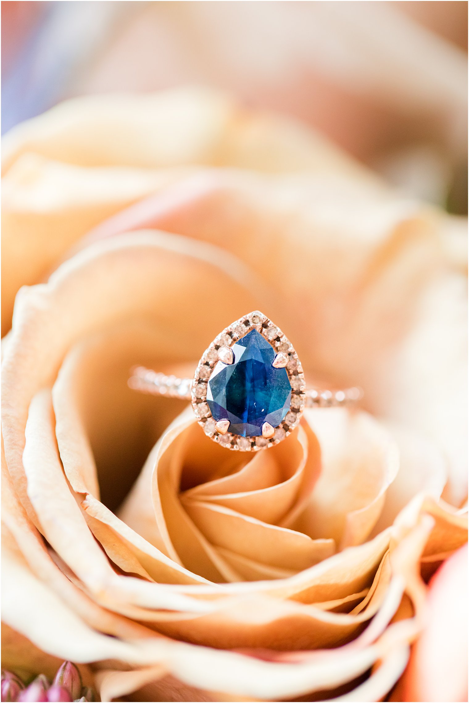 custom wedding ring with blue stone rests on peach rose