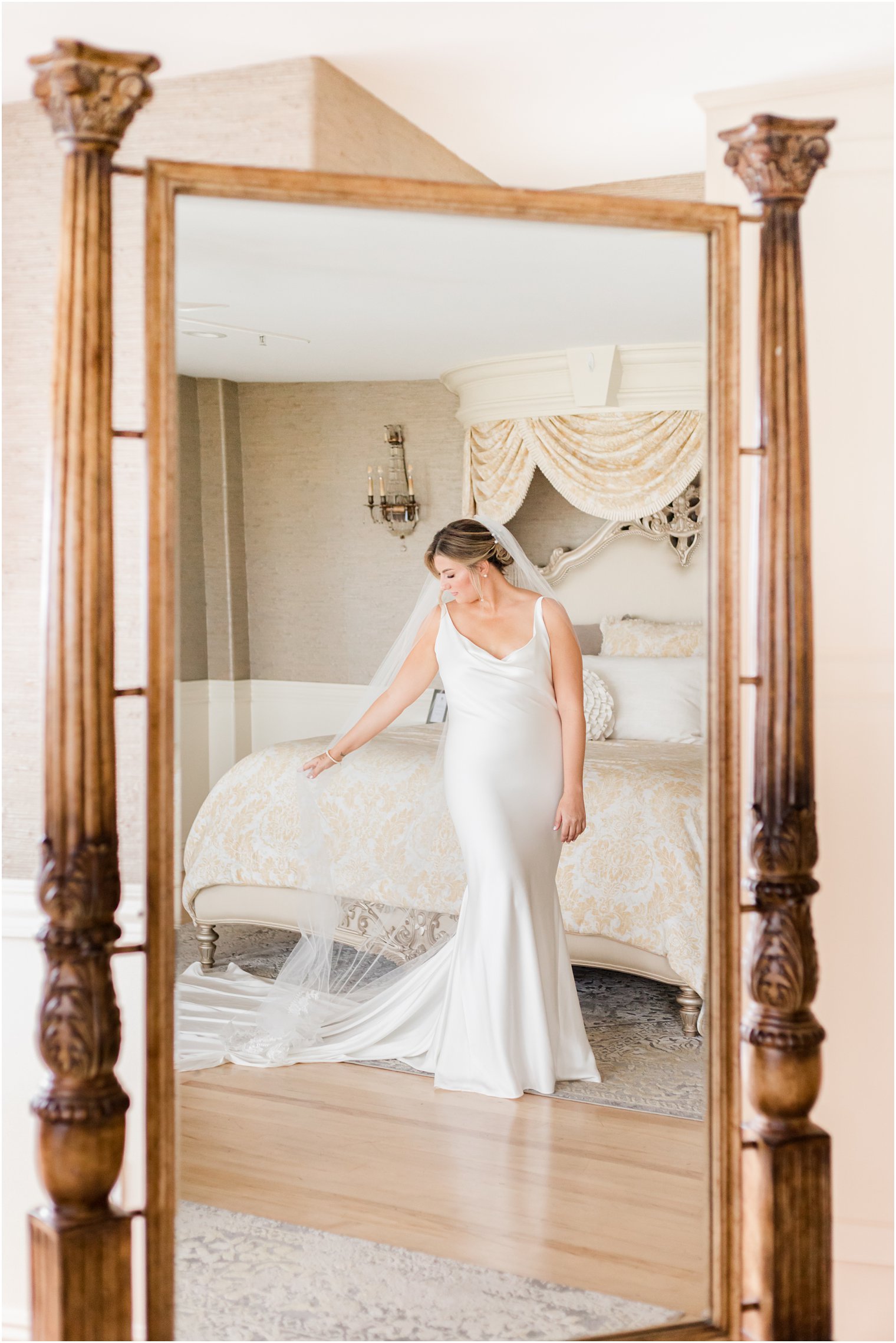 bride stands by bed in bridal suite at Bonnet Island Estate with veil behind her