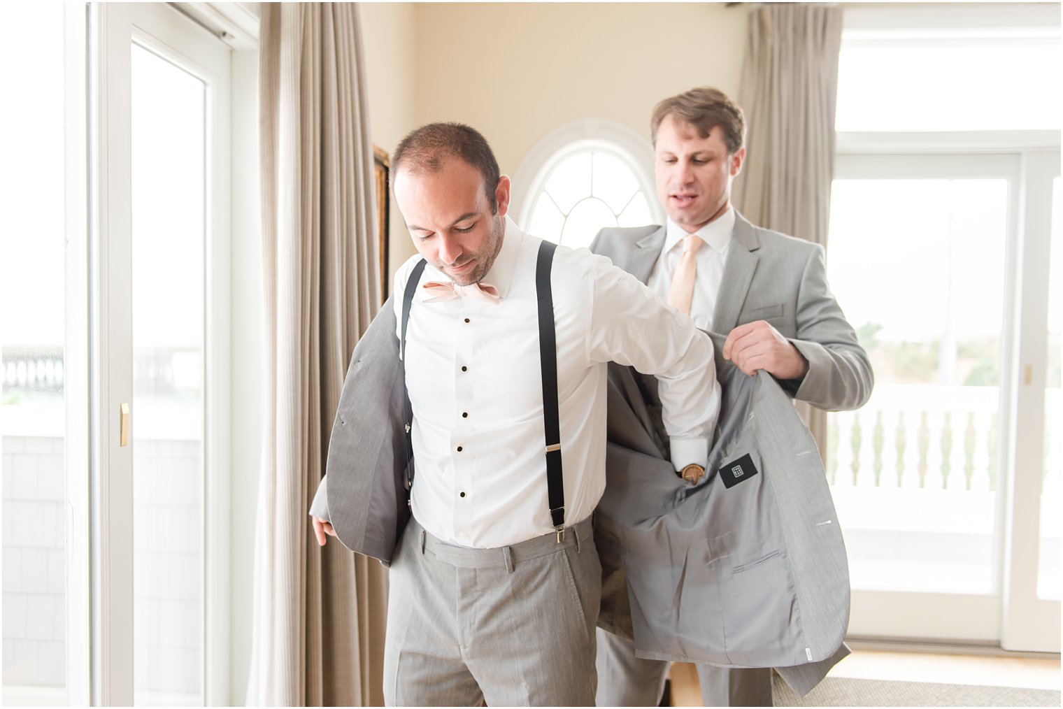 groomsman helps groom into suit jacket before NJ wedding