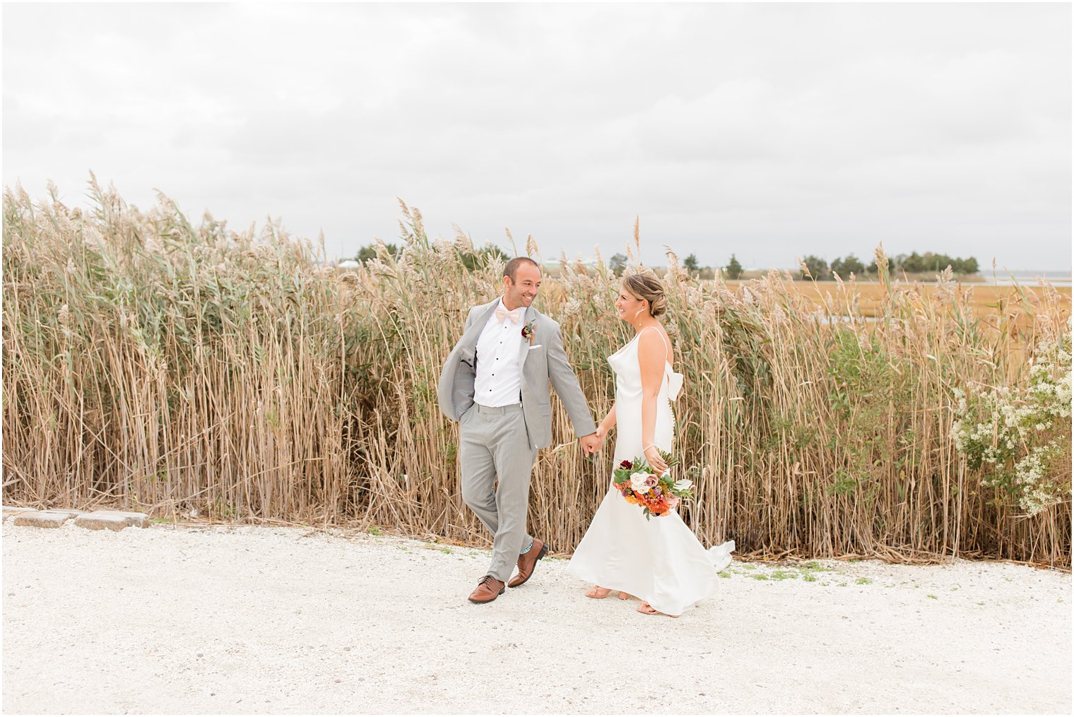 newlyweds hold hands walking through sand in Manahawkin NJ