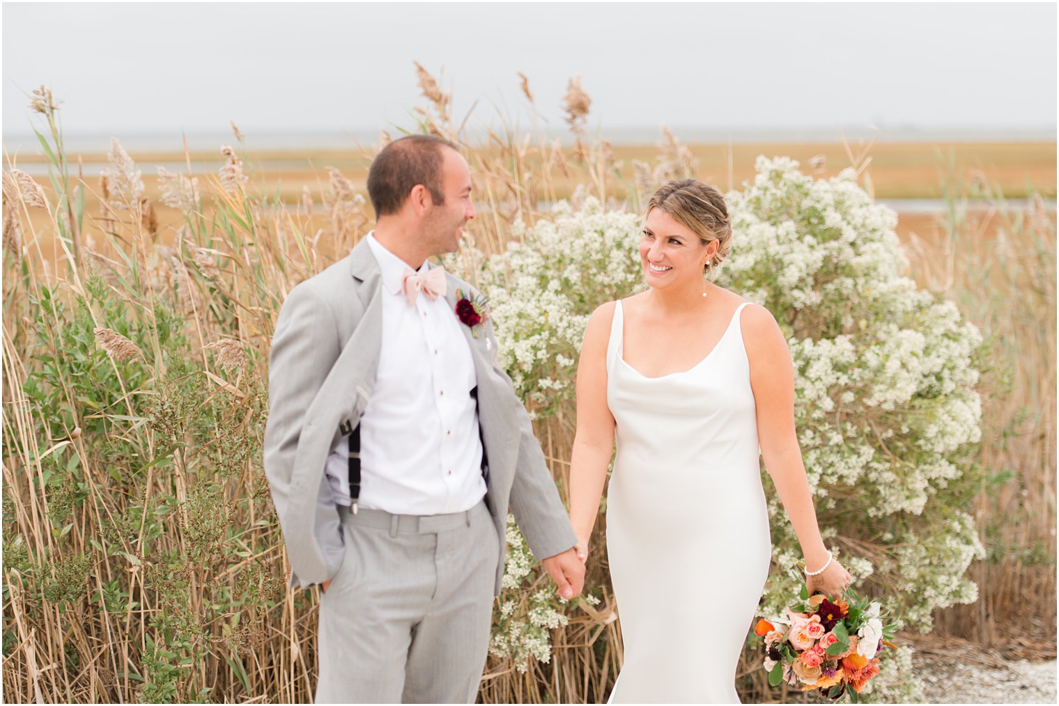 bride and groom hold hands walking along tall grass at Bonnet Island Estate