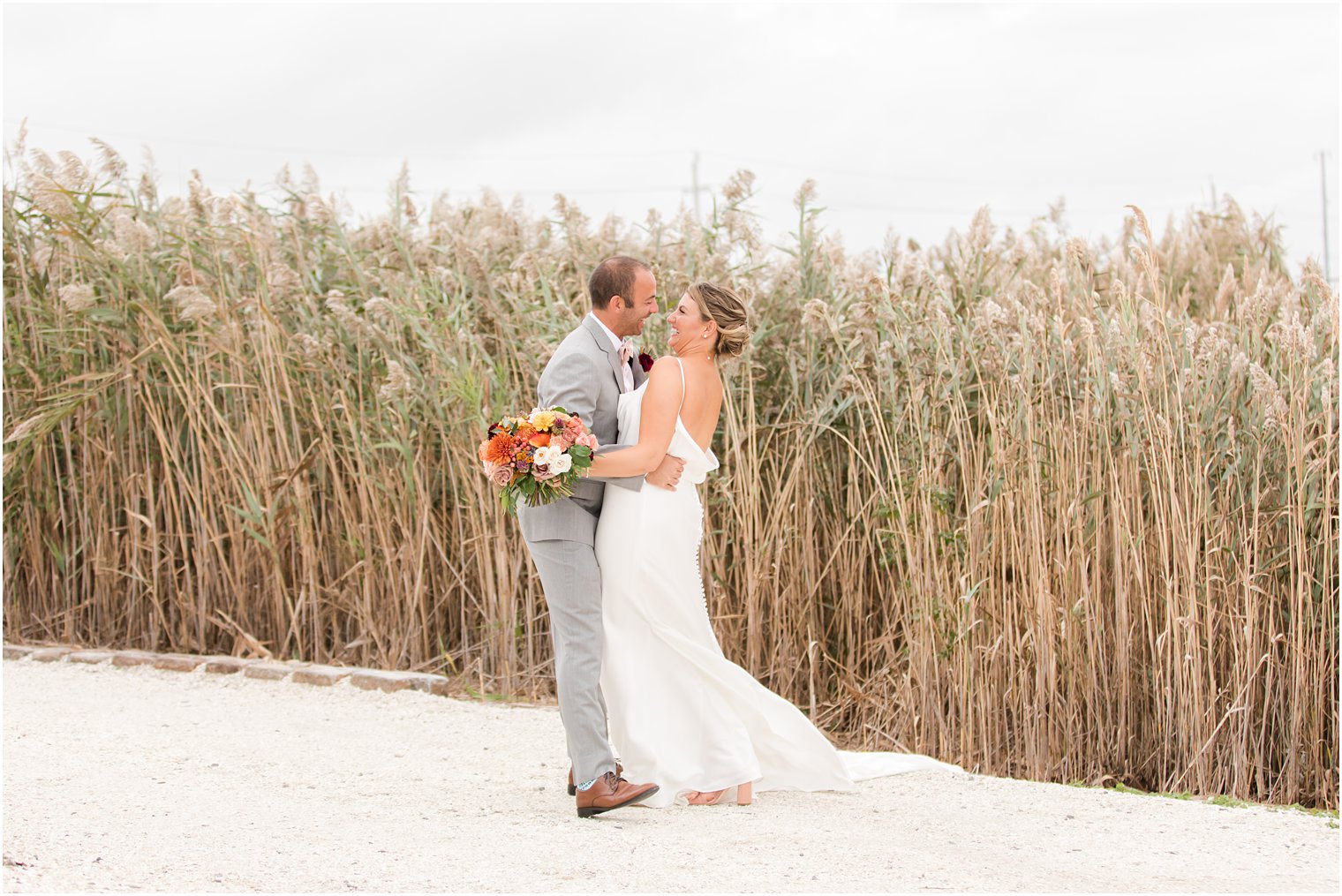 newlyweds laugh by tall grass on beach in Manahawkin NJ