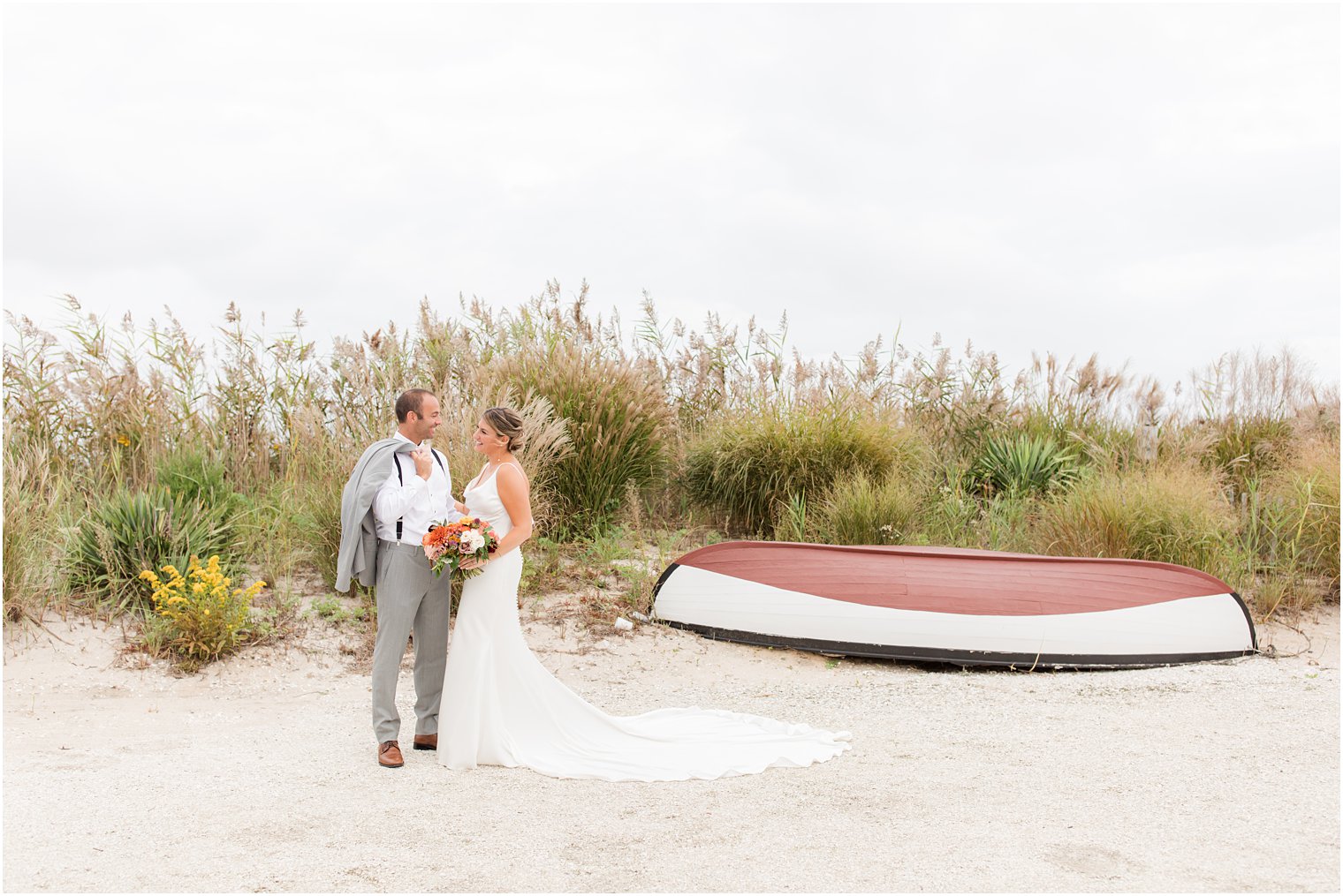 bride and groom stand by boat on beach in Manahawkin NJ 