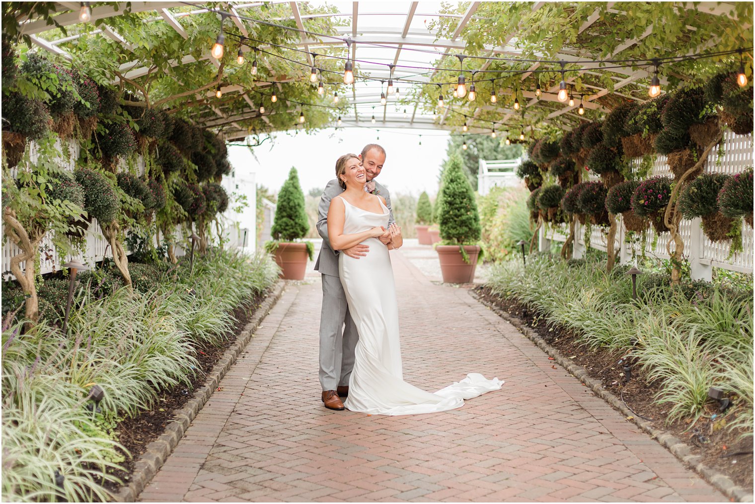 bride and groom hug in gardens under bistro lights on wedding day