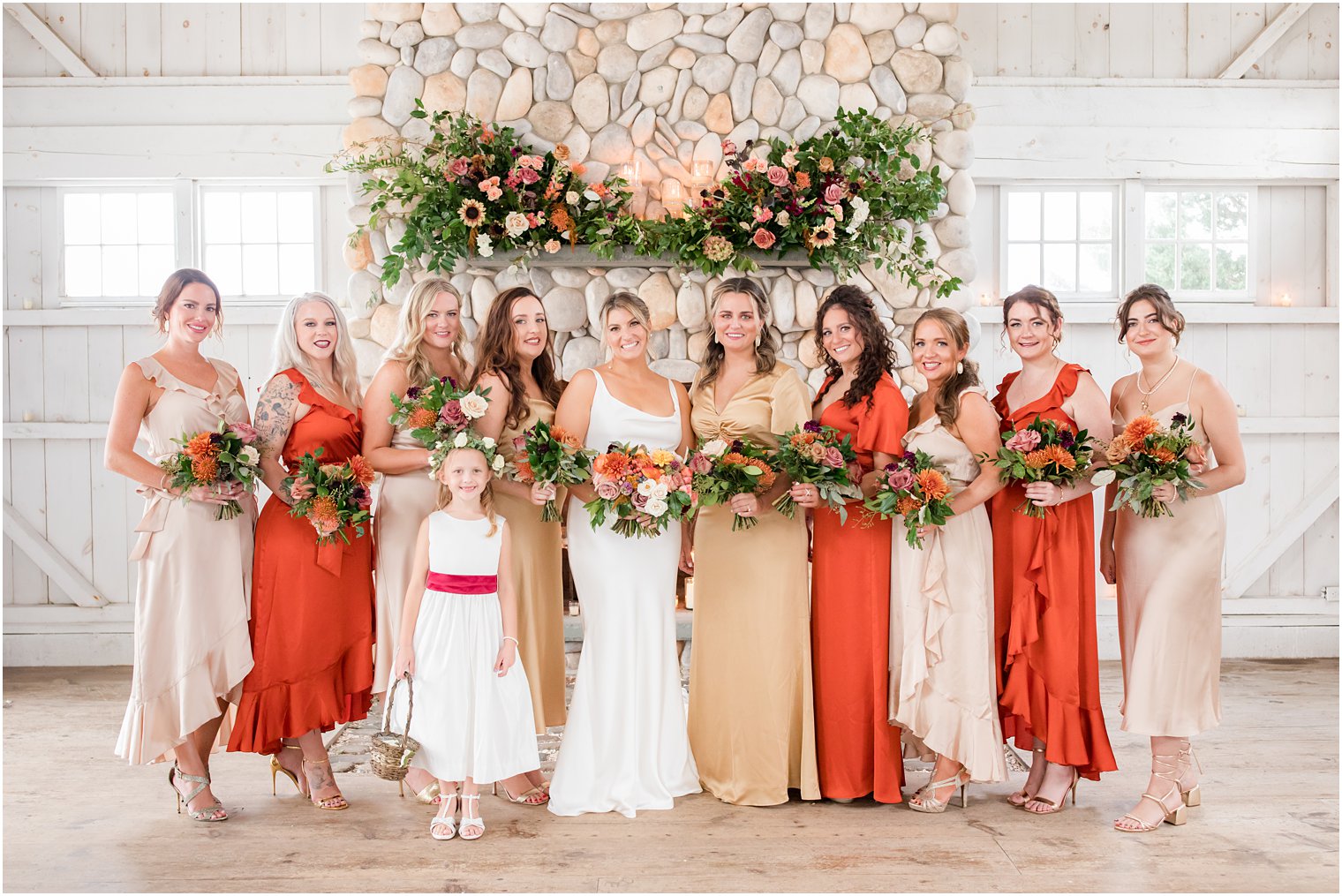 bride stands with bridesmaids in mismatched gowns in orange and gold