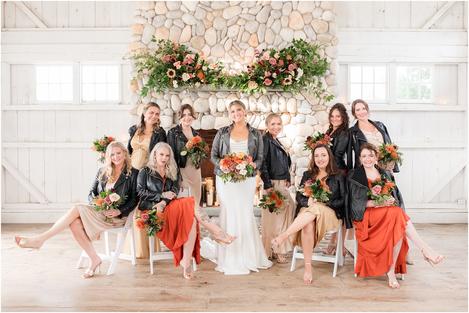 bride poses with bridesmaids in mismatched fall dresses with leather jackets