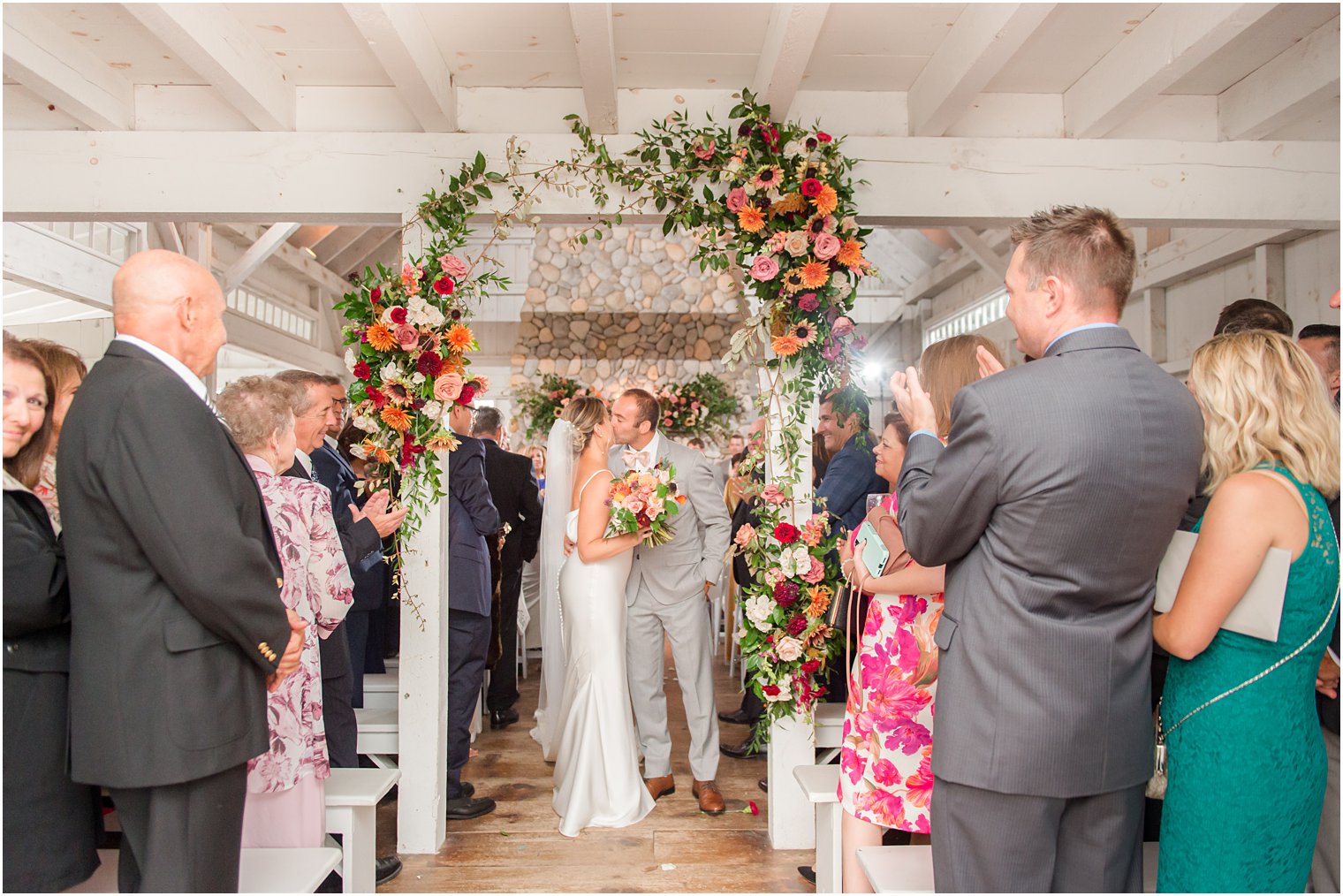 newlyweds kiss under floral arbor after ceremony in Bonnet Island Estate barn