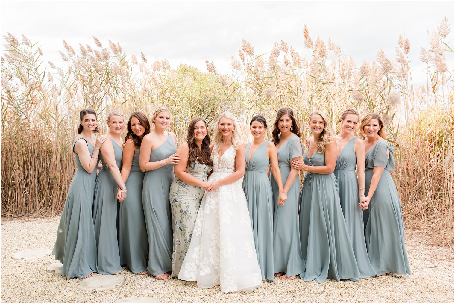 bride and bridesmaids in dusty blue gowns pose by tall grass on Brant Beach 