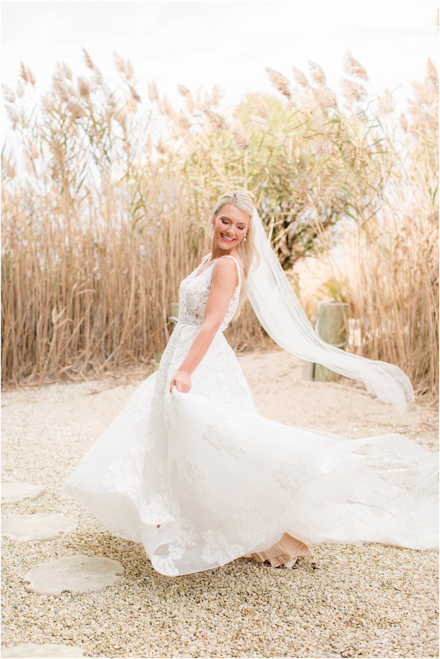 bride smiles twirling wedding gown with her veil floating behind her on Brant Beach in New Jersey 