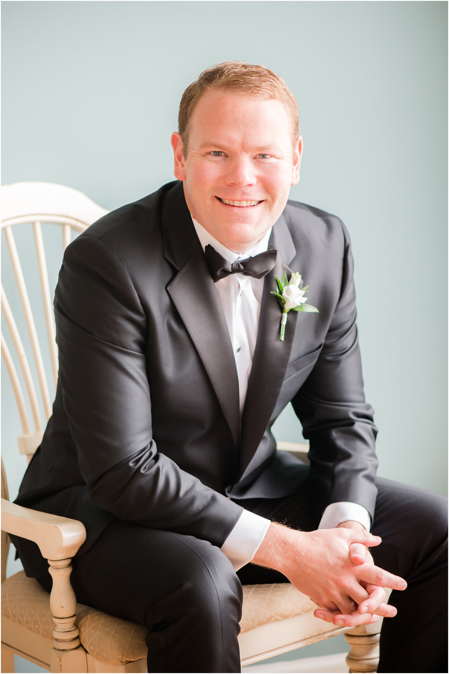 groom sits in chair at Brant Beach Yacht Club smiling 