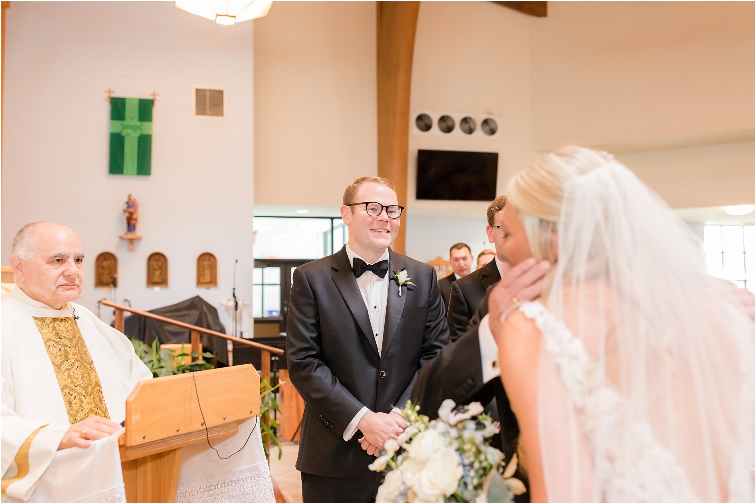 groom smiles at bride while dad gives her away during traditional church wedding in New Jersey