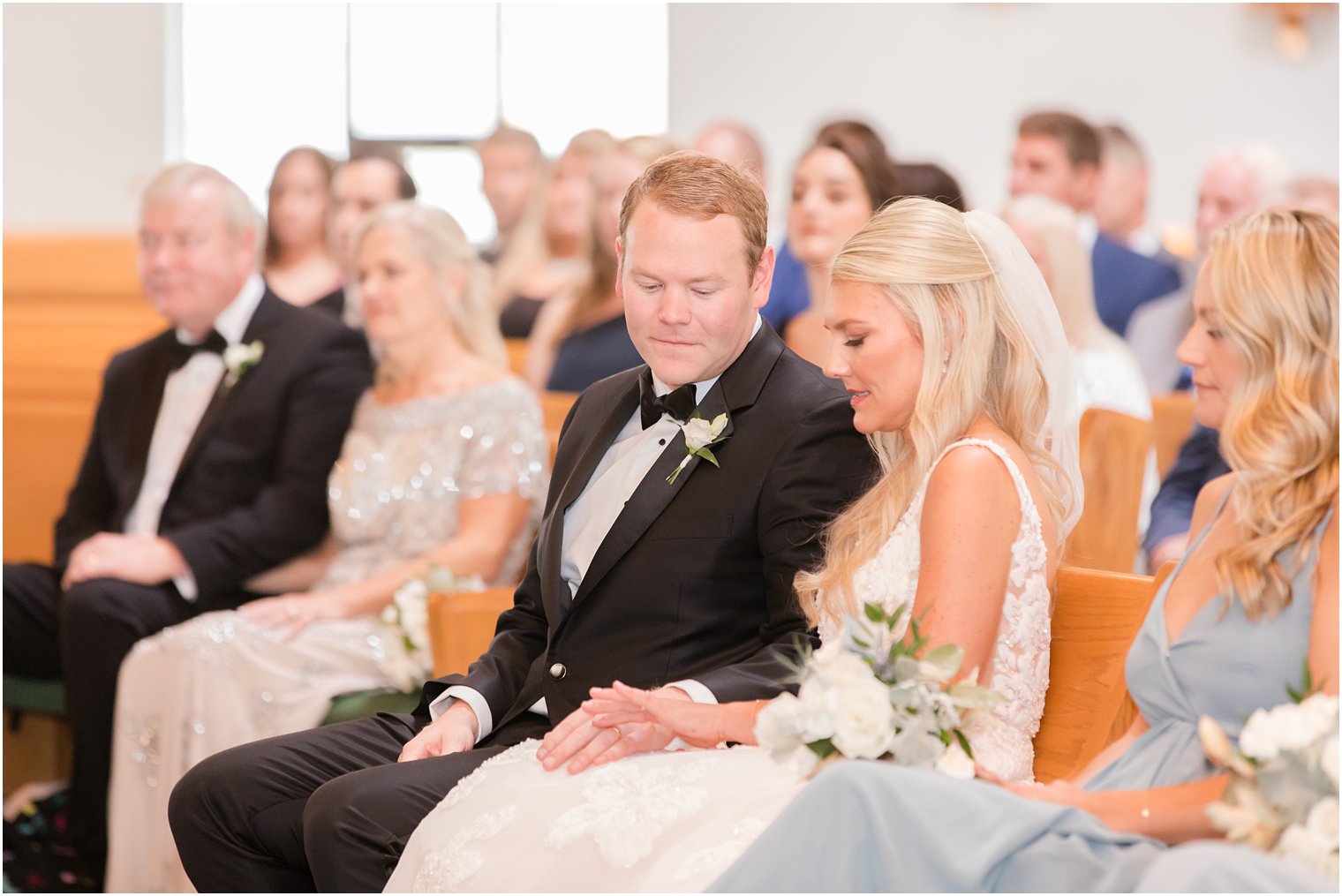 bride and groom sit in pew during traditional church wedding in New Jersey