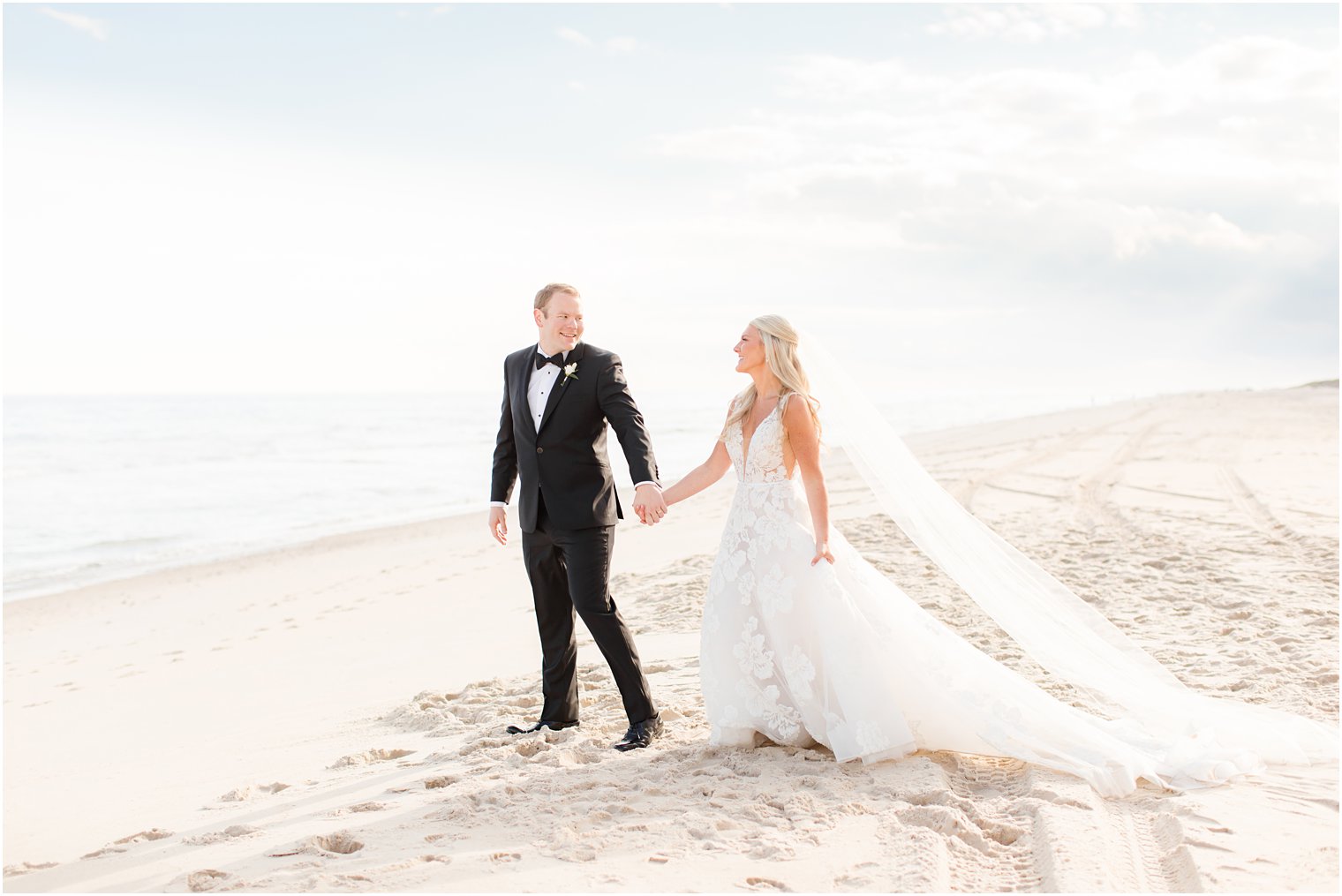 groom holds bride's hand leading her on the beach 