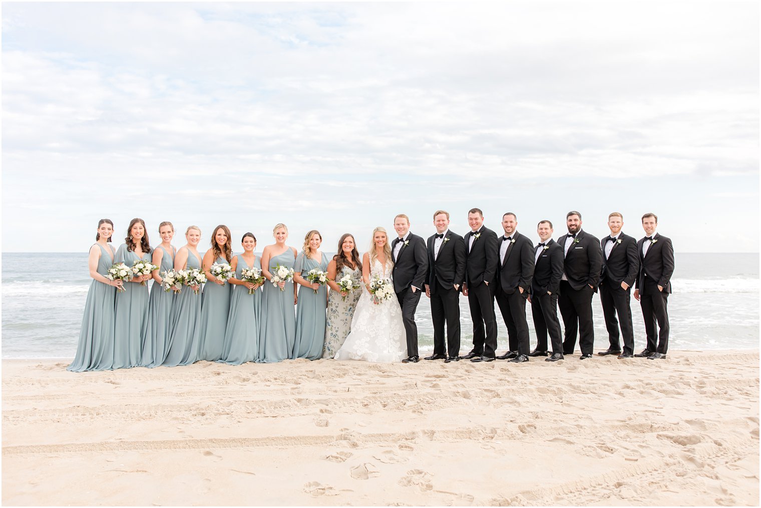 bride and groom stand with bridal party in black tuxes and dusty blue gowns 