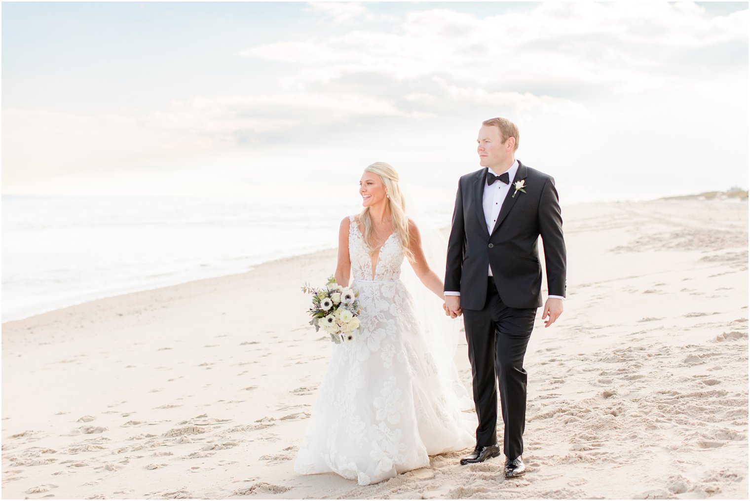 bride and groom hold hands walking on the beach in Long Beach NJ