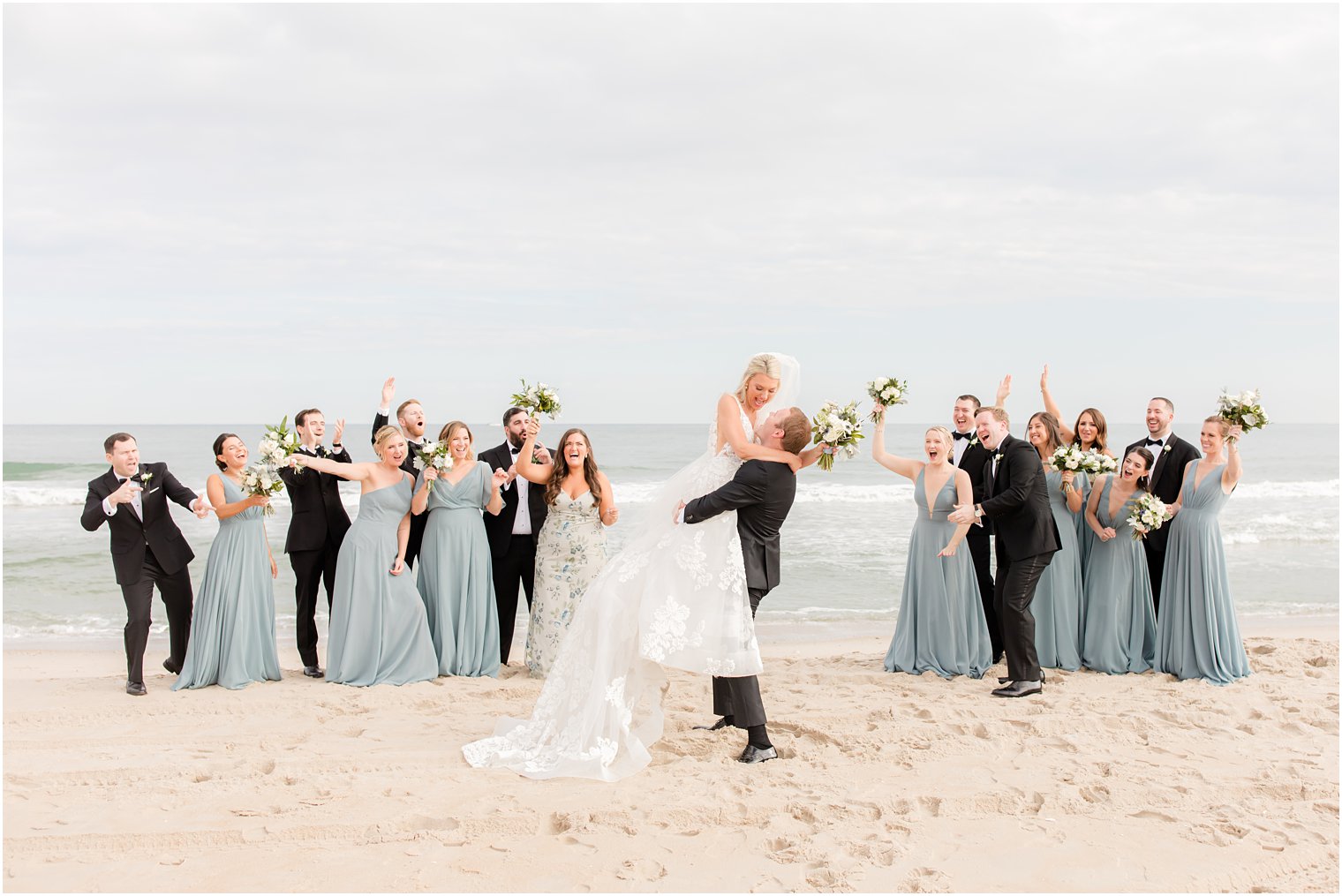 groom smiles at bride while lifting her in the air as bridal party cheers