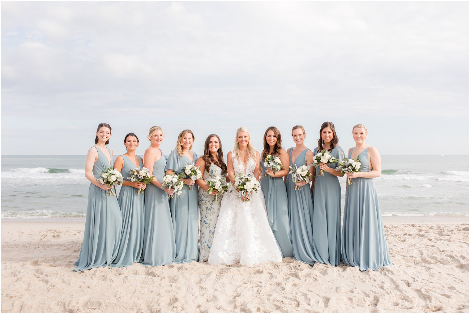 bride stands with bridesmaids in light blue gowns on beach for fall wedding day
