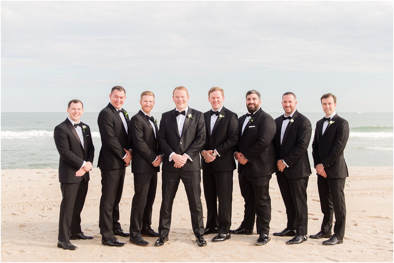 groomsmen stand with groom in classic black tuxes on the beach 