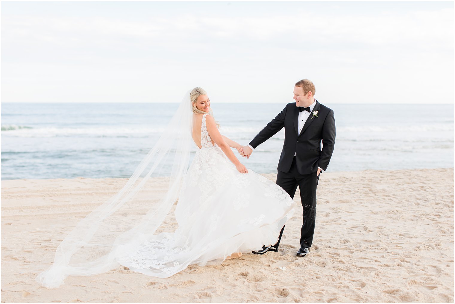 groom looks at bride showing off wedding gown on the beach 