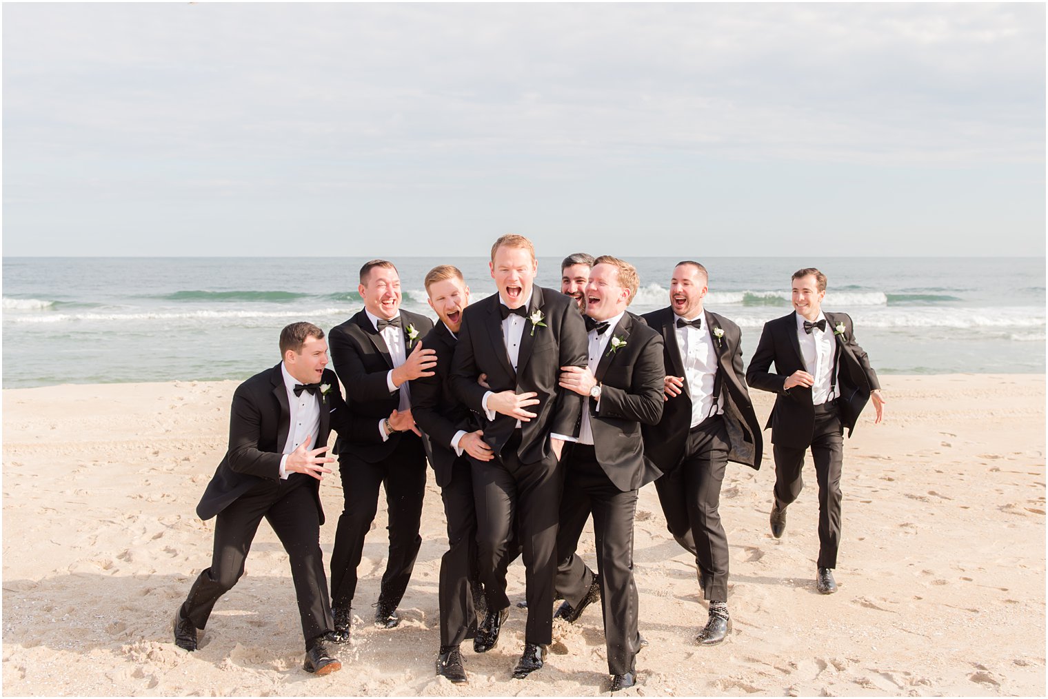 groomsmen run up and hug groom on Brant Beach 