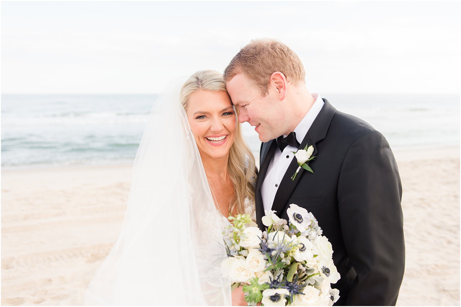 groom nuzzles bride's cheek on beach laughing on wedding day 