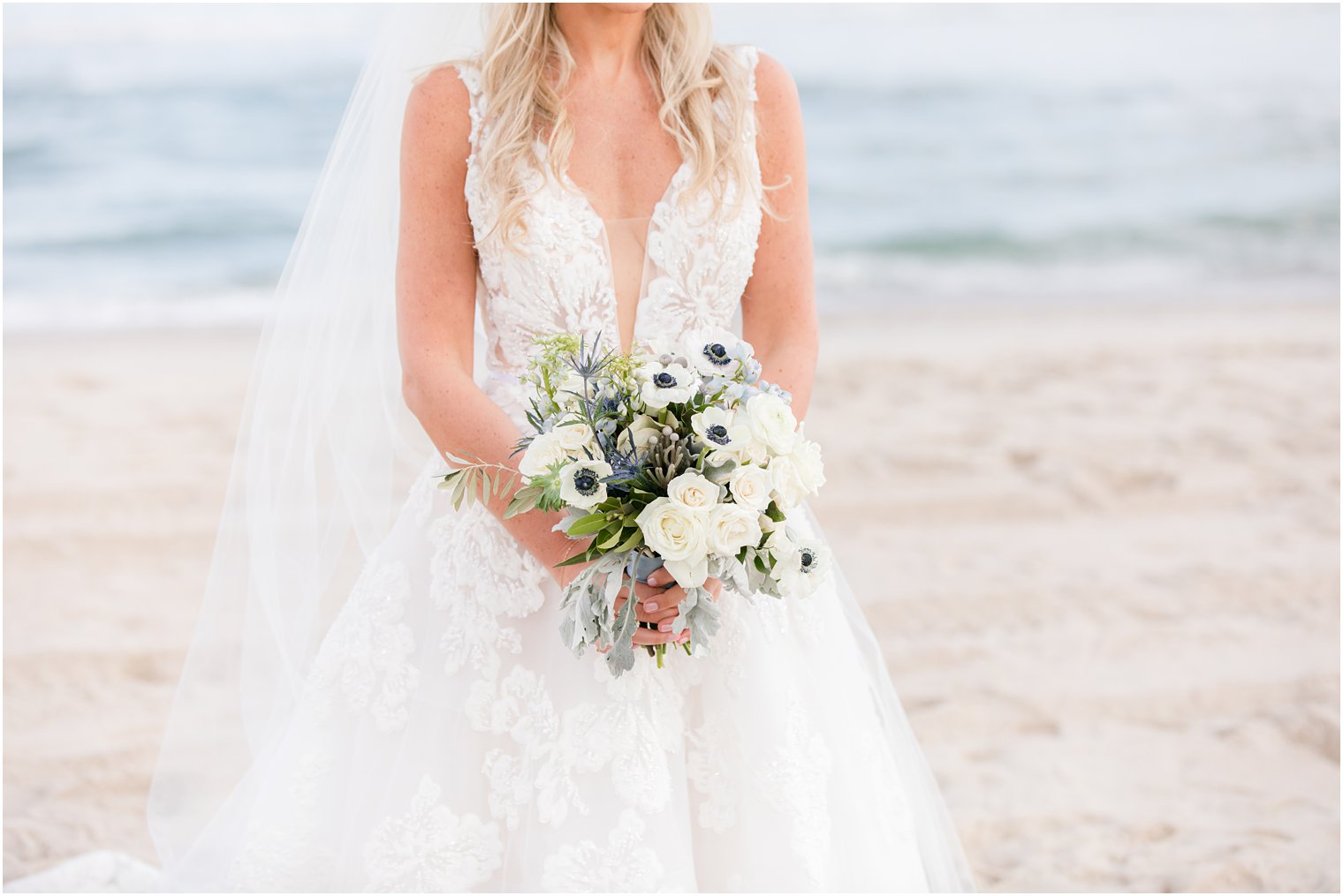 bride holds bouquet of white flowers on the beach for fall wedding day