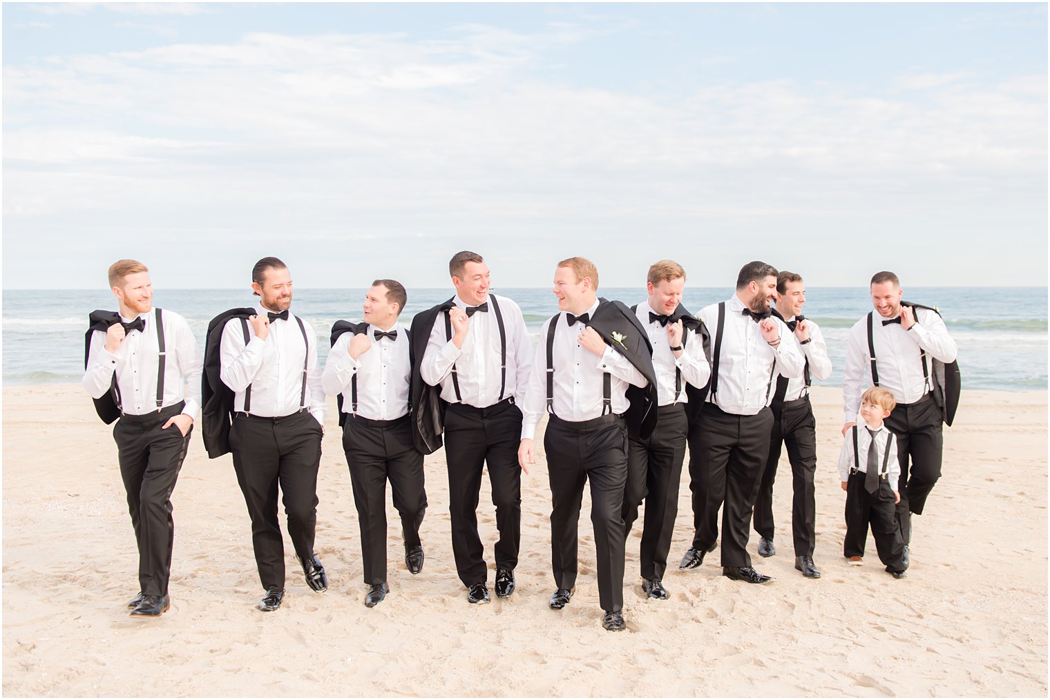 groom walks with groomsmen in tuxes at Brant Beach