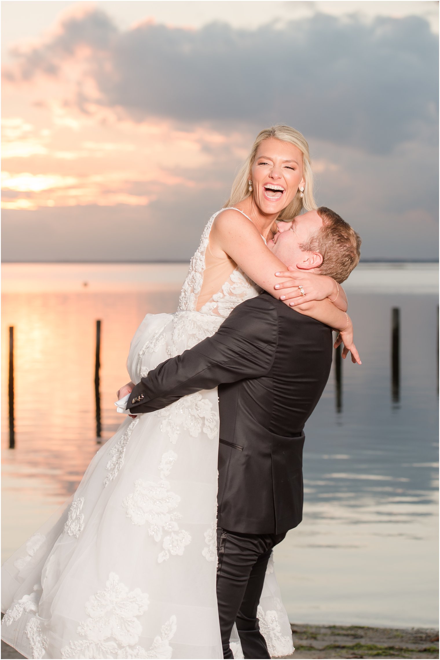 groom lifts bride up on beach at sunset in New Jersey 