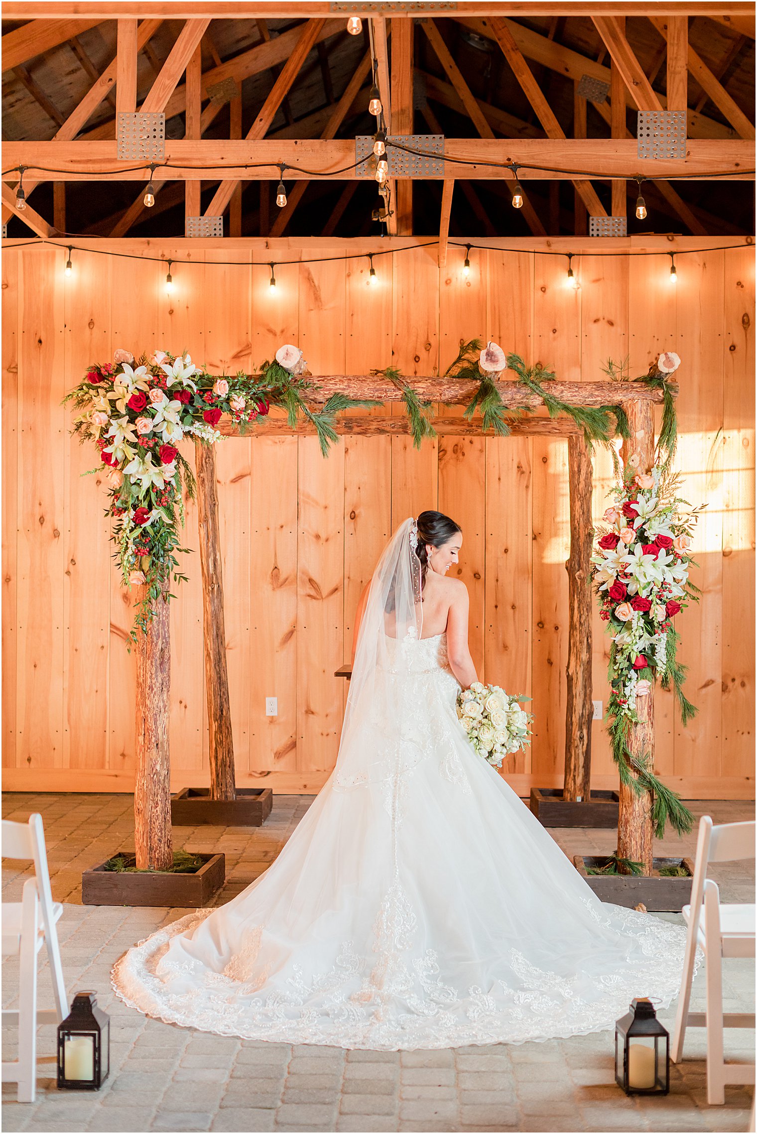 bride poses under wooden arbor with red and white flowers 
