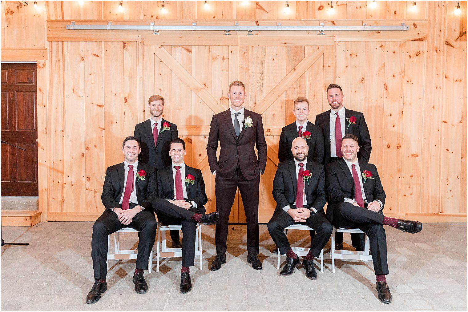 groom stands with groomsmen in black suits with red ties 